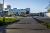 an empty parking lot surrounded by tall buildings and green grass in front of it, surrounded by two rows of trees