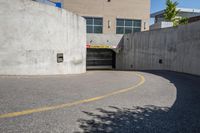 an empty parking space with yellow lines and no cars on it in the background, and building with concrete walls