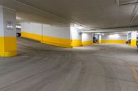 an empty parking space with yellow painted walls and concrete flooring and two cars parked