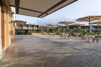 an empty patio with several white table and chairs under umbrellas in an outdoor area