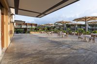 an empty patio with several white table and chairs under umbrellas in an outdoor area