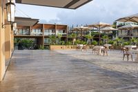 an empty patio with several white table and chairs under umbrellas in an outdoor area