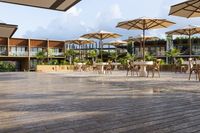 an empty patio with several white table and chairs under umbrellas in an outdoor area