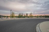 an empty paved road with multiple poles by water at sunset or dawn on a cloudy day