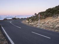 an empty winding road on a mountain with the sun set above the mountains in the background