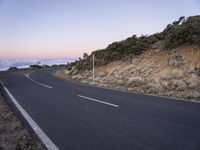 an empty winding road on a mountain with the sun set above the mountains in the background