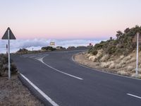 an empty winding road on a mountain with the sun set above the mountains in the background