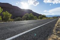 an empty paved road in front of some mountains and bushes and trees on either side