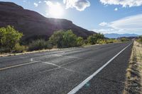 an empty paved road in front of some mountains and bushes and trees on either side