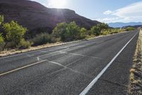 an empty paved road in front of some mountains and bushes and trees on either side