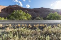 an empty paved road in front of some mountains and bushes and trees on either side