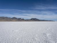 white snow is spread across the flat surface of an empty plain, with mountains in background