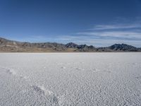 white snow is spread across the flat surface of an empty plain, with mountains in background