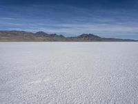 white snow is spread across the flat surface of an empty plain, with mountains in background