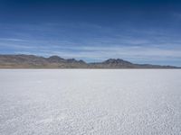 white snow is spread across the flat surface of an empty plain, with mountains in background