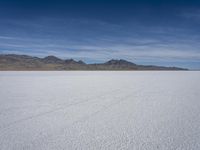 white snow is spread across the flat surface of an empty plain, with mountains in background