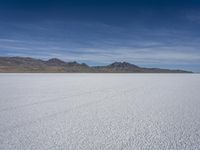 white snow is spread across the flat surface of an empty plain, with mountains in background