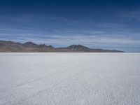 white snow is spread across the flat surface of an empty plain, with mountains in background