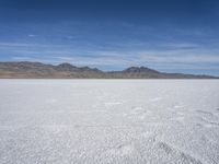 white snow is spread across the flat surface of an empty plain, with mountains in background