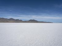 white snow is spread across the flat surface of an empty plain, with mountains in background