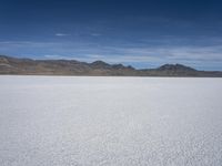 white snow is spread across the flat surface of an empty plain, with mountains in background