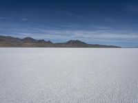 white snow is spread across the flat surface of an empty plain, with mountains in background