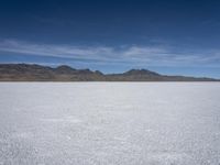 white snow is spread across the flat surface of an empty plain, with mountains in background