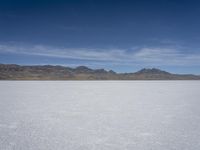 white snow is spread across the flat surface of an empty plain, with mountains in background