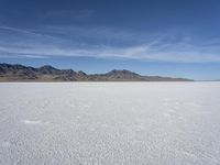 white snow is spread across the flat surface of an empty plain, with mountains in background