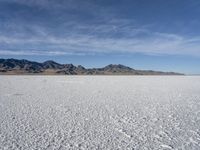 white snow is spread across the flat surface of an empty plain, with mountains in background