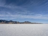 white snow is spread across the flat surface of an empty plain, with mountains in background