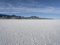 white snow is spread across the flat surface of an empty plain, with mountains in background