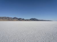 white snow is spread across the flat surface of an empty plain, with mountains in background