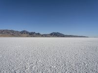 white snow is spread across the flat surface of an empty plain, with mountains in background