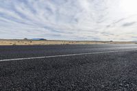 a motorcycle is parked near an empty stretch of asphalt in an empty plain with a bright sky