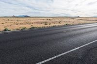 a motorcycle is parked near an empty stretch of asphalt in an empty plain with a bright sky