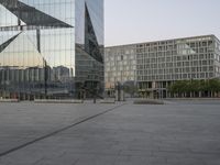 an empty plaza in front of a glass building with trees in the foreground and blue skies