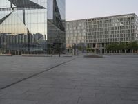 an empty plaza in front of a glass building with trees in the foreground and blue skies