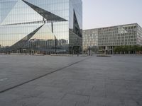 an empty plaza in front of a glass building with trees in the foreground and blue skies