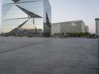 an empty plaza in front of a glass building with trees in the foreground and blue skies