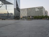 an empty plaza in front of a glass building with trees in the foreground and blue skies