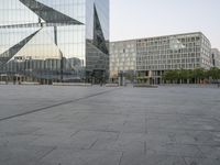 an empty plaza in front of a glass building with trees in the foreground and blue skies