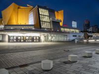 an empty plaza lit up at night with buildings in the background with blue skies and blue and yellow lights