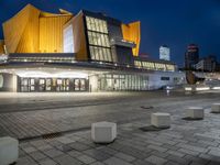 an empty plaza lit up at night with buildings in the background with blue skies and blue and yellow lights