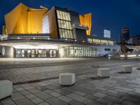 an empty plaza lit up at night with buildings in the background with blue skies and blue and yellow lights