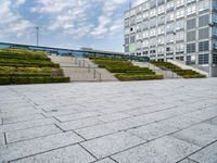 an empty plaza with steps leading to a building and a tower in the distance outside