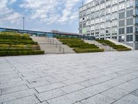 an empty plaza with steps leading to a building and a tower in the distance outside