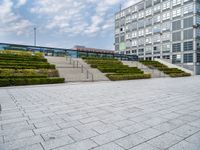 an empty plaza with steps leading to a building and a tower in the distance outside