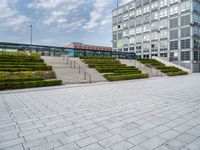 an empty plaza with steps leading to a building and a tower in the distance outside