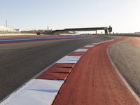 an empty track with red and blue stripes near a highway with a bridge in the background